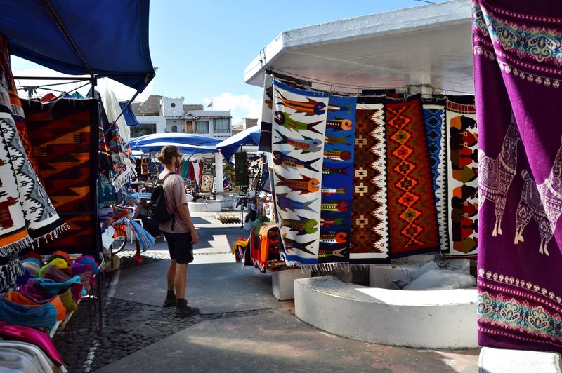 Мужчина выбирает цветной текстиль на рынке в Отавало