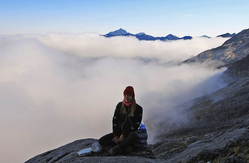 Девушка сидит на фоне облаков высоко в горах