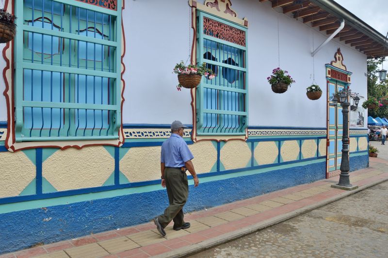 Пожилой мужчина идет вдоль голубой стены