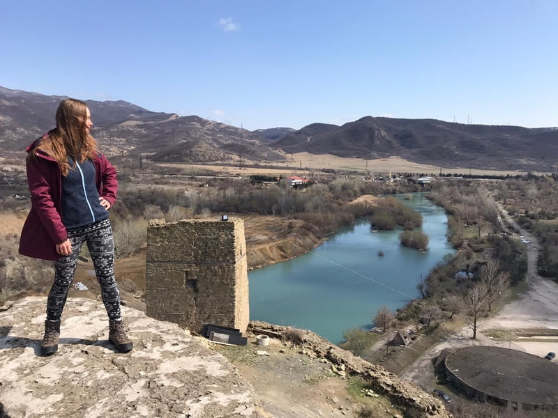 Девушка смотрит на реку стоя на стене разрушенной крепости