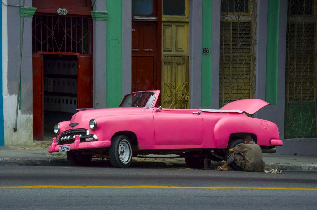 Кубинец ремонтирует колесо розового автомобиля