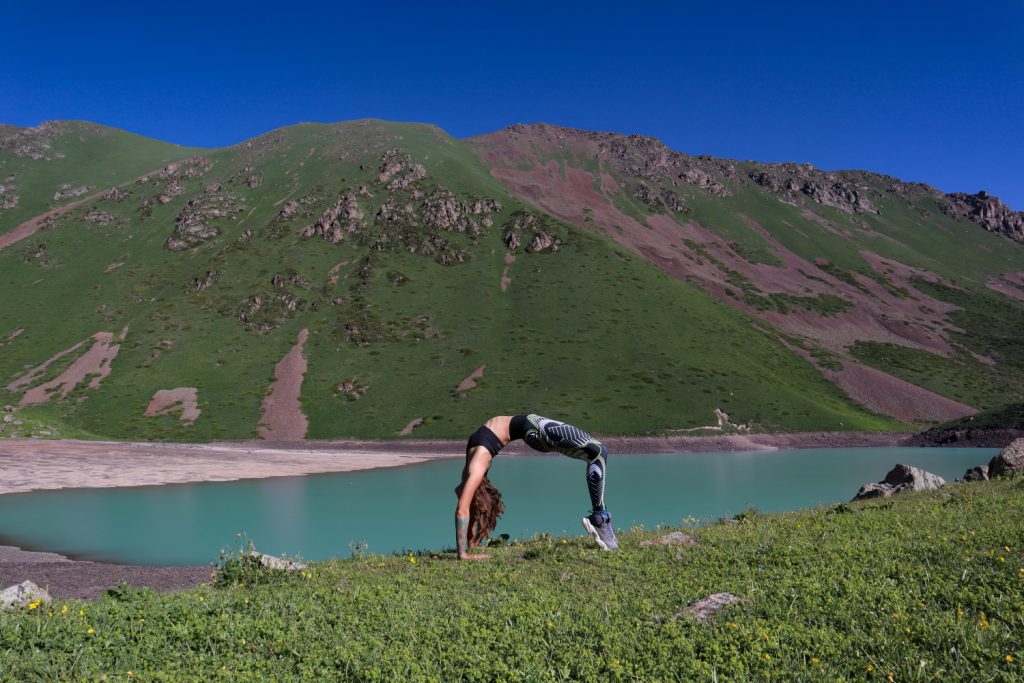девушка делает мостик на фоне голубого водоема и гор