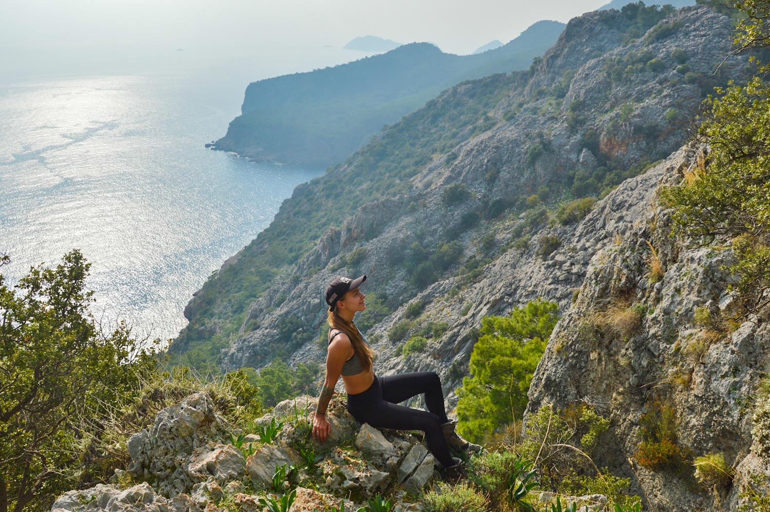 Девушка позирует на вершине горы с видом на море