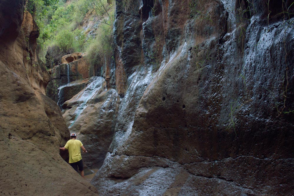 Парень в желтой футболке пробирается между узких стен каньона