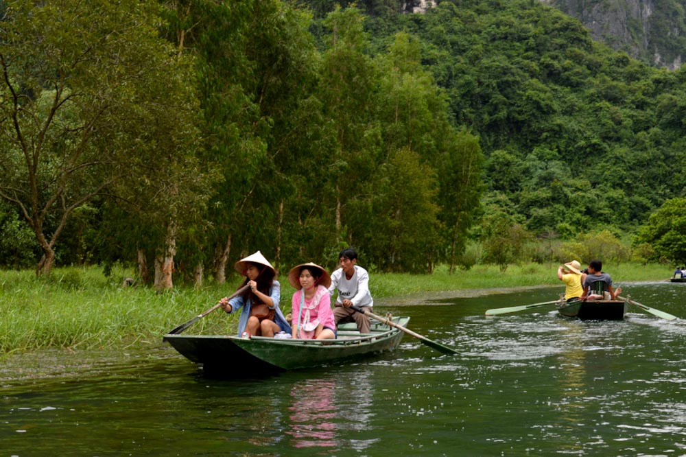Туристы в вьетнамских шляпах управляют лодкой