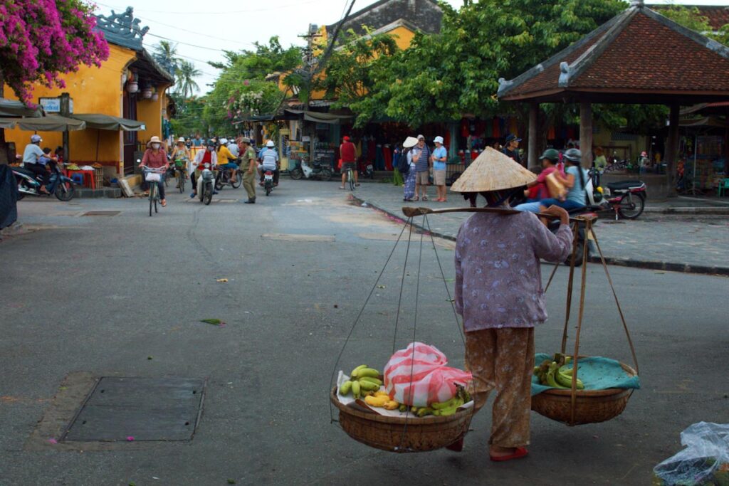 Женщина во вьетнамском костюме и шляпе несет корыто с фруктами