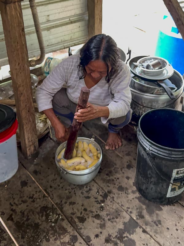 Женщина сидит на корточках и мешает палкой бананы в кастрюле / Woman squatting and mixing bananas in a pot